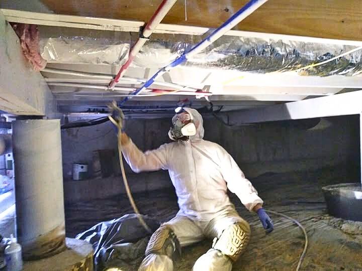 Original photograph: TLC Land Crew mold remediation technician in full Tyvek PPE suit, respirator, and knee pads kneeling under floor joists during a crawl space mold remediation job in Southwest Missouri