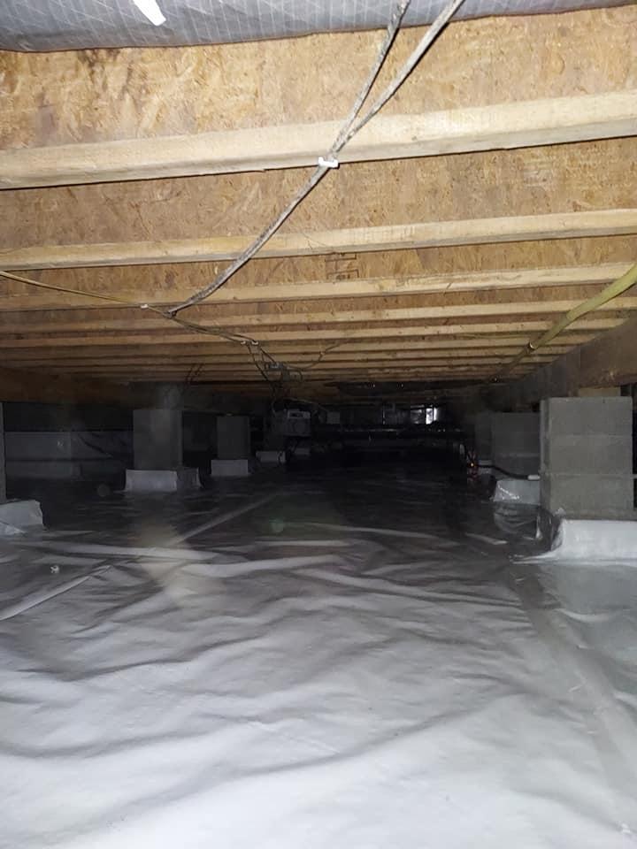 Original photograph: a fully encapsulated crawl space with clean floor joists overhead and a sealed white vapor barrier covering the floor and walls