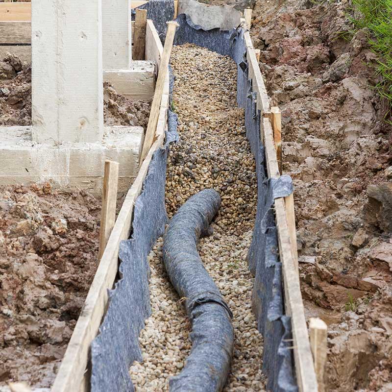 French drain trench with perforated pipe and gravel along a foundation