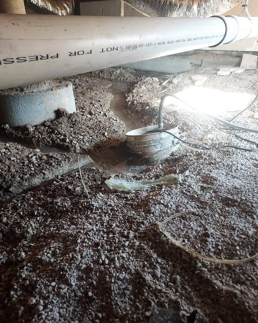 Original photograph: an old sump pump sitting on bare dirt in a contaminated crawl space, surrounded by debris and pipe penetrations